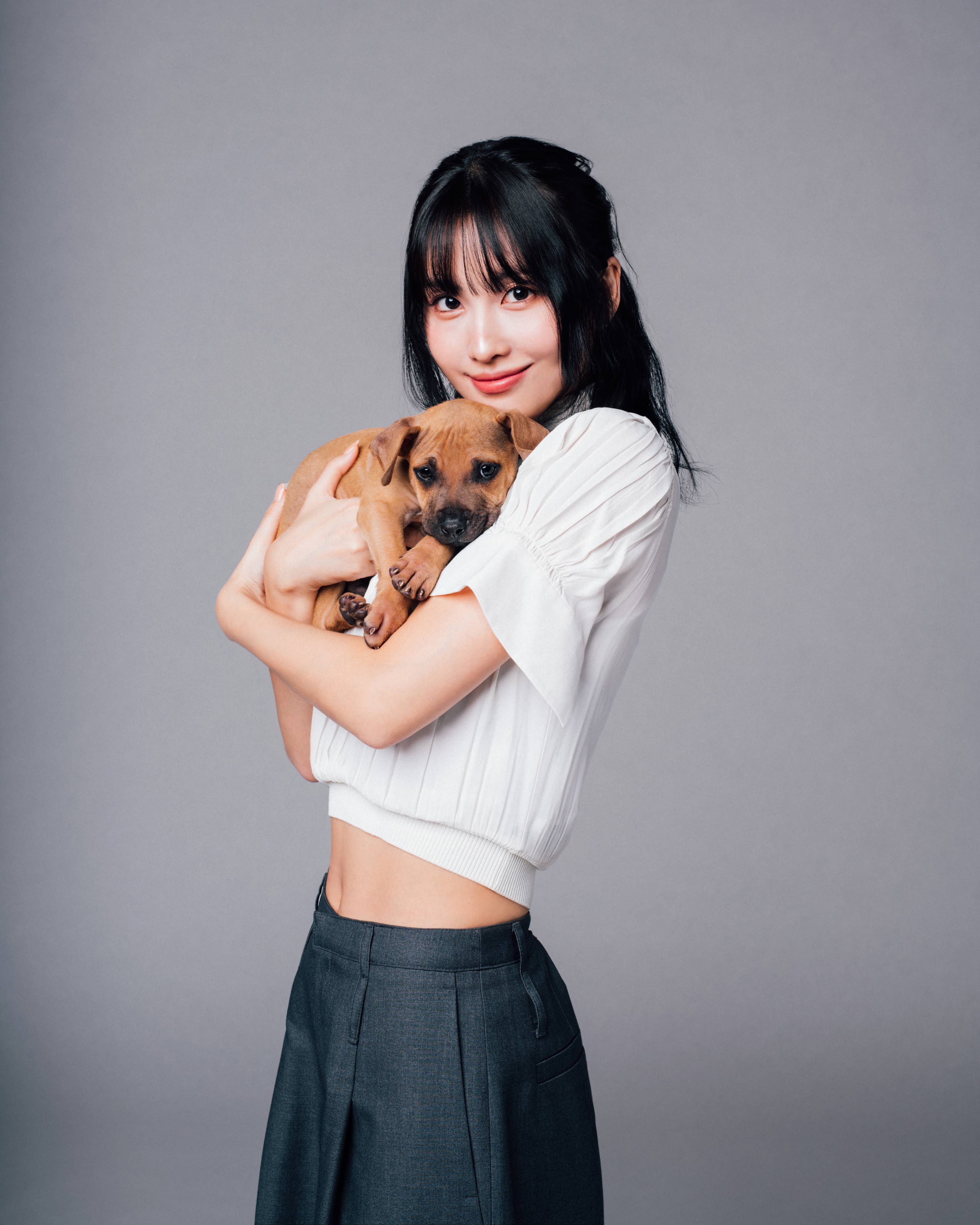 Woman in a cropped top and high-waisted pants holding a small puppy