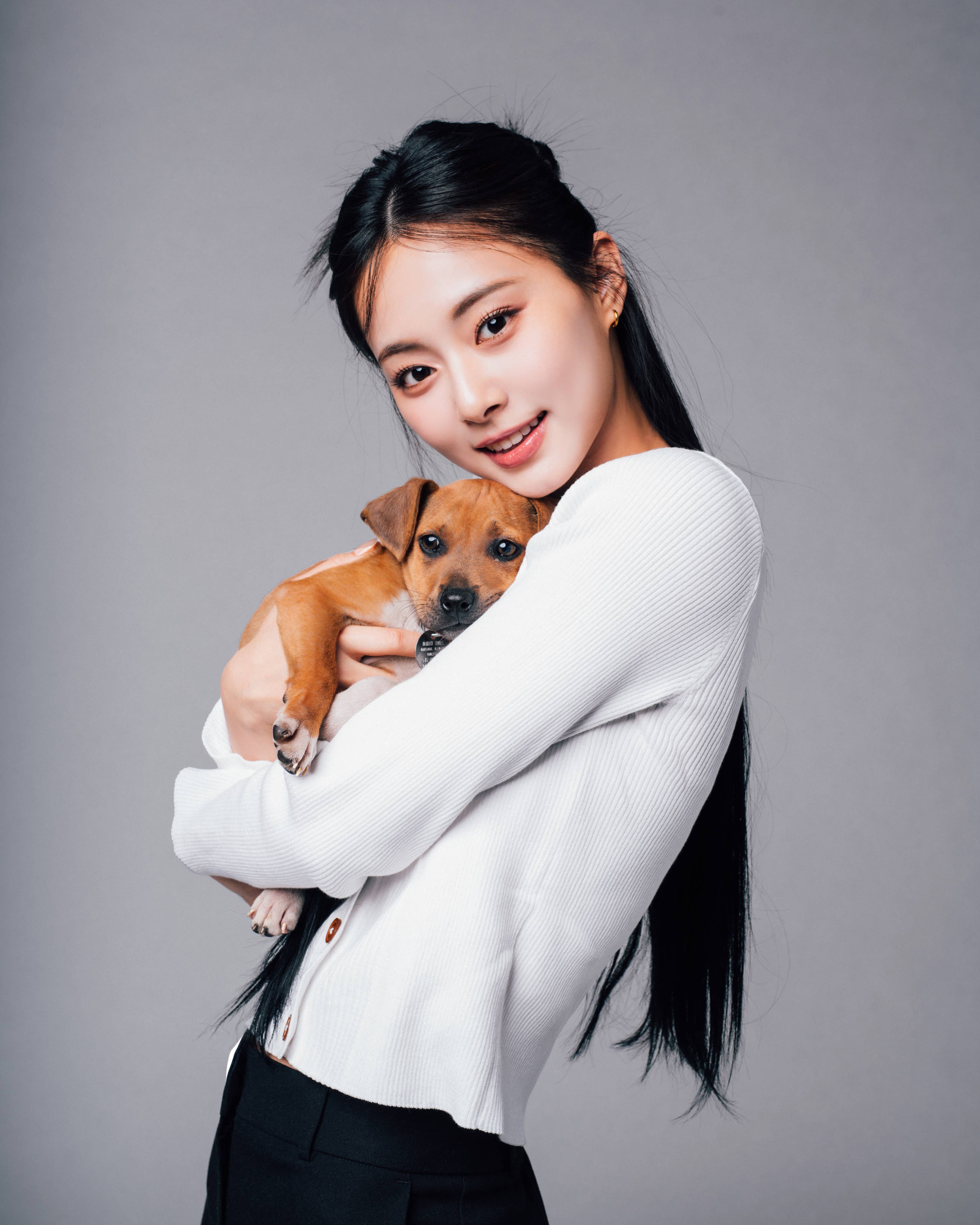 Woman in a white top holds a small puppy, both looking at the camera