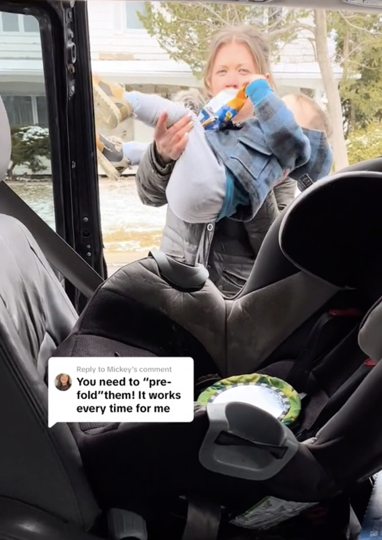 Woman demonstrates folding technique with baby clothes near a car seat; text bubble: &quot;You need to &#x27;pre-fold&#x27; them! It works every time for me&quot;