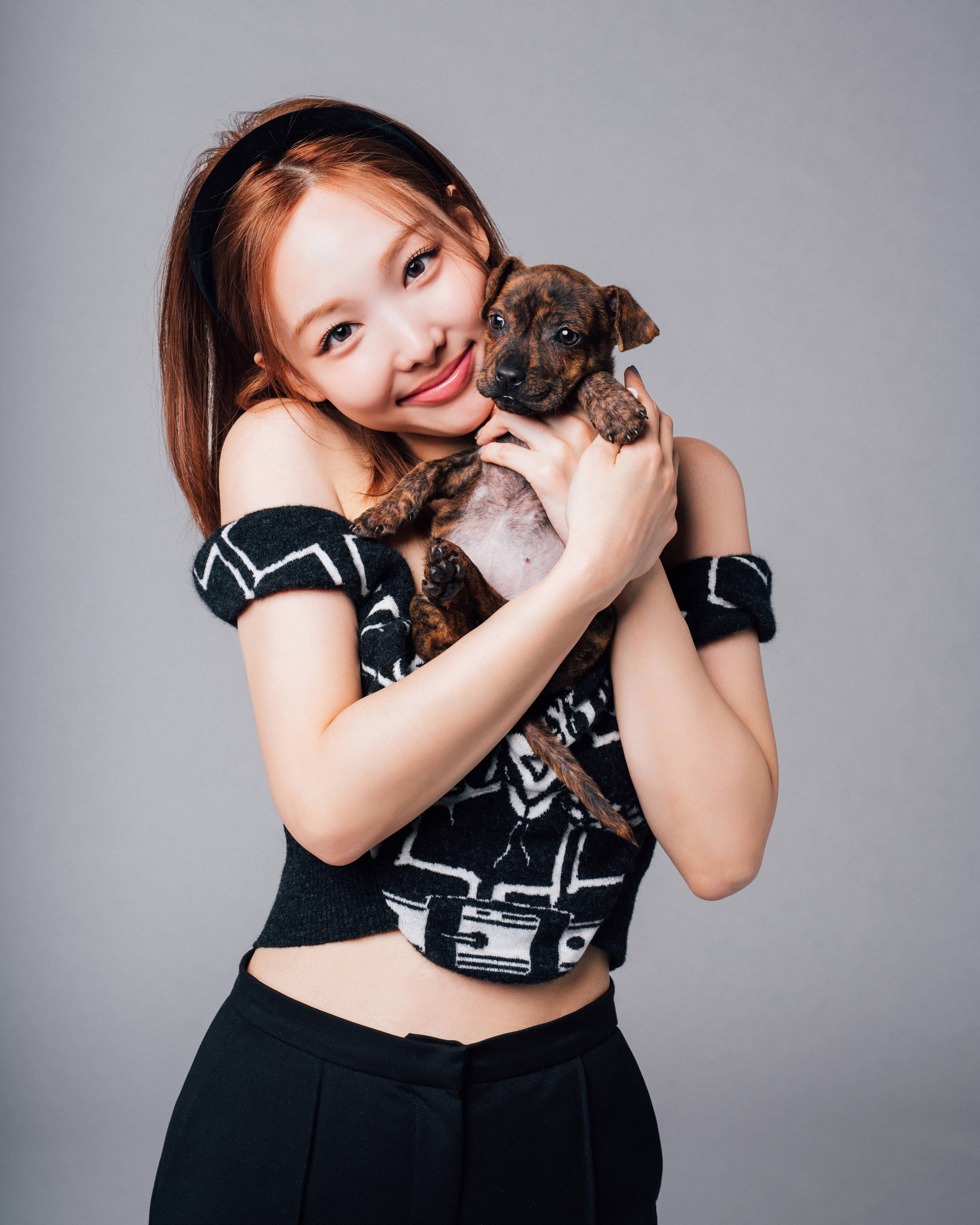 Young woman smiling, holding a small puppy, wearing a patterned top and high-waisted pants