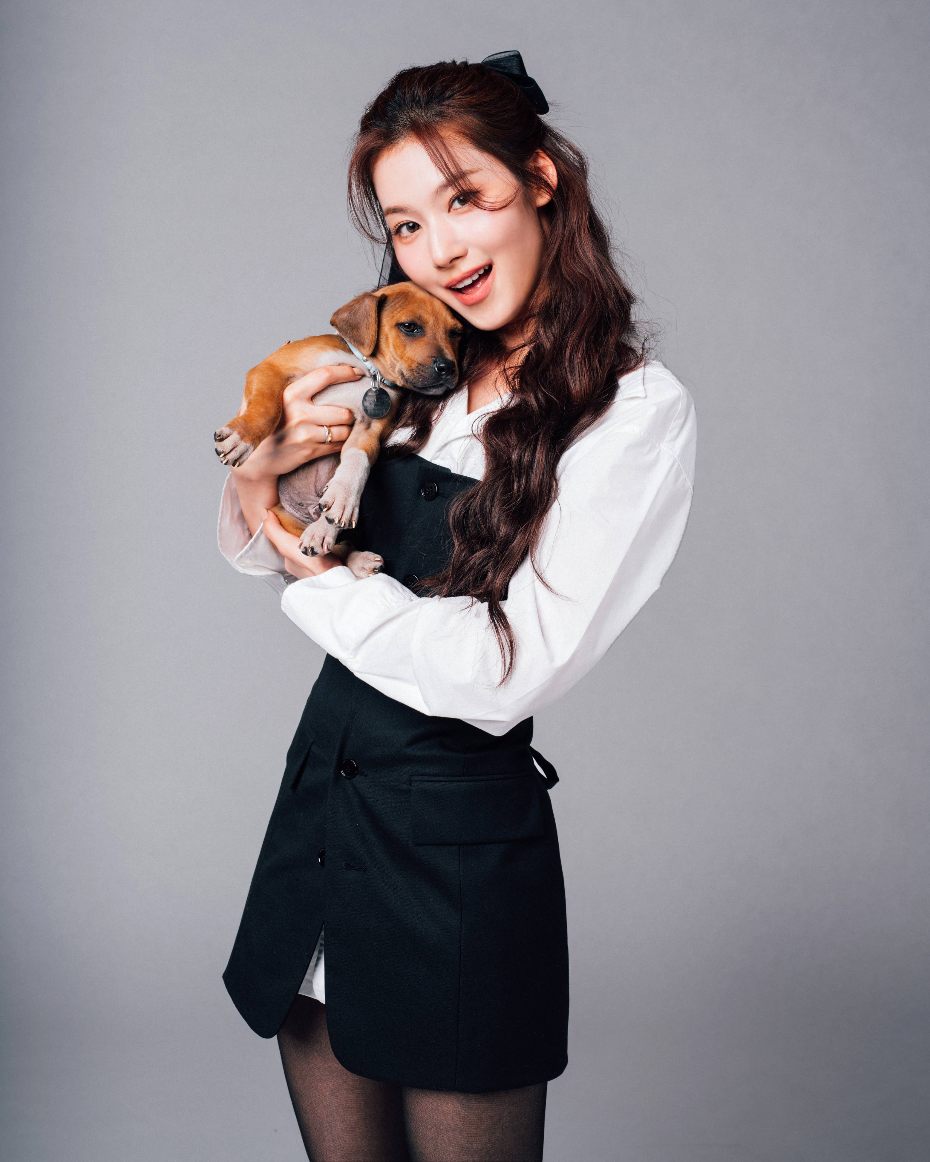 Woman holding a puppy, wearing a business casual outfit with a bow in her hair