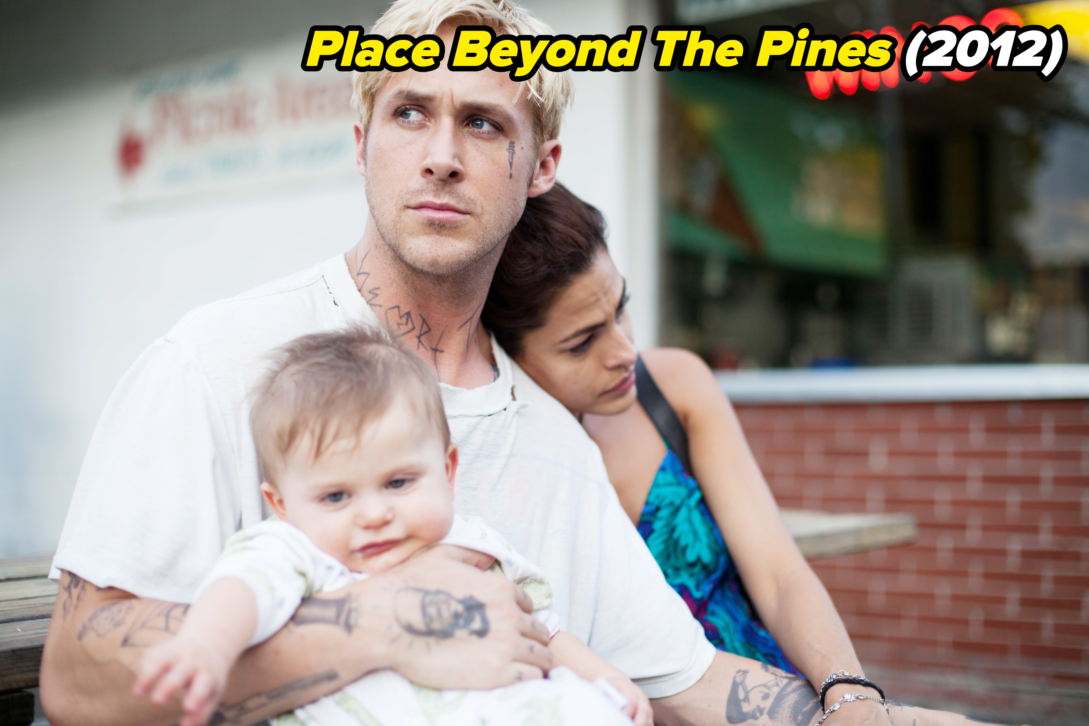 Ryan is sitting and holding a baby as Eva leans on him in a scene from The Place Beyond The Pines