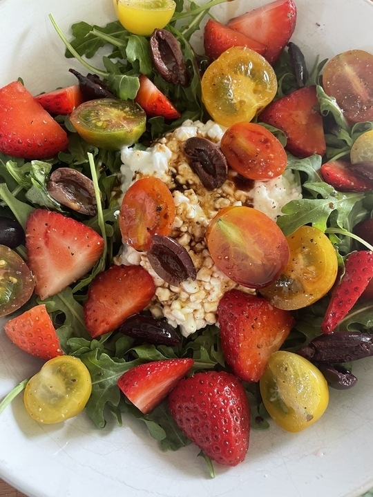 A fresh salad with strawberries, various tomatoes, greens, and cheese in a white bowl