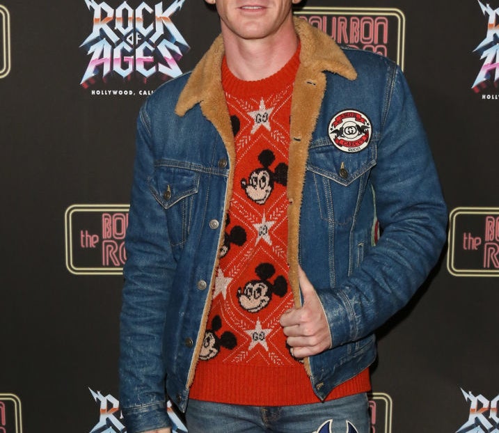 Closeup of Drake Bell on the red carpet wearing a denim jacket and a sweater with a Mickey Mouse motif
