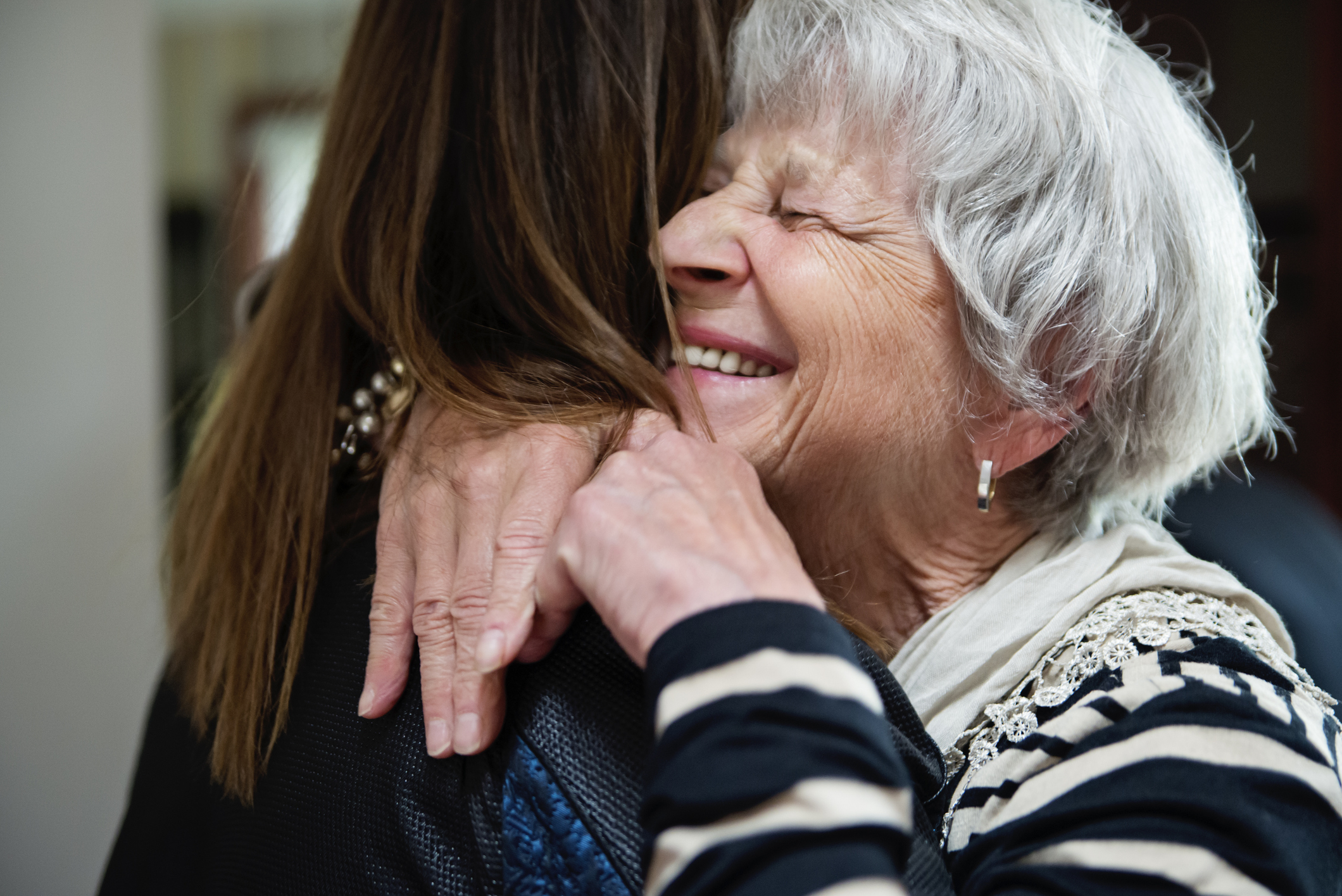 Elderly woman embracing a younger woman, both smiling, conveying a warm, familial bond