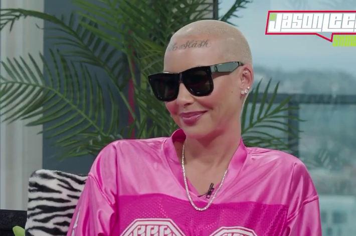 Amber Rose in sunglasses, buzz cut with tattoo, wearing a pink sports jersey, smiling during an interview
