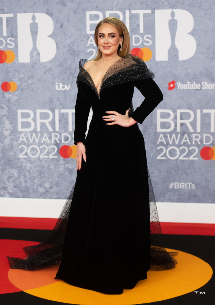 Adele in a low-cut long sleeved gown with a tulle over-layer and collar