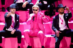Three performers in pink suits with cowboy hats sitting on steps, one holding a microphone