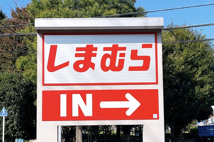 駐車場入口の標識で、「しまむら IN →」と書かれています。