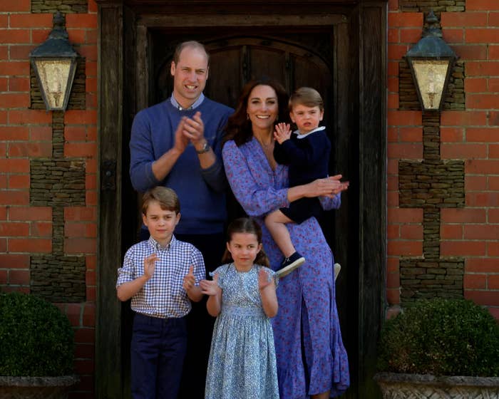 prince william and kate with their 3 kids posing in front of a doorway