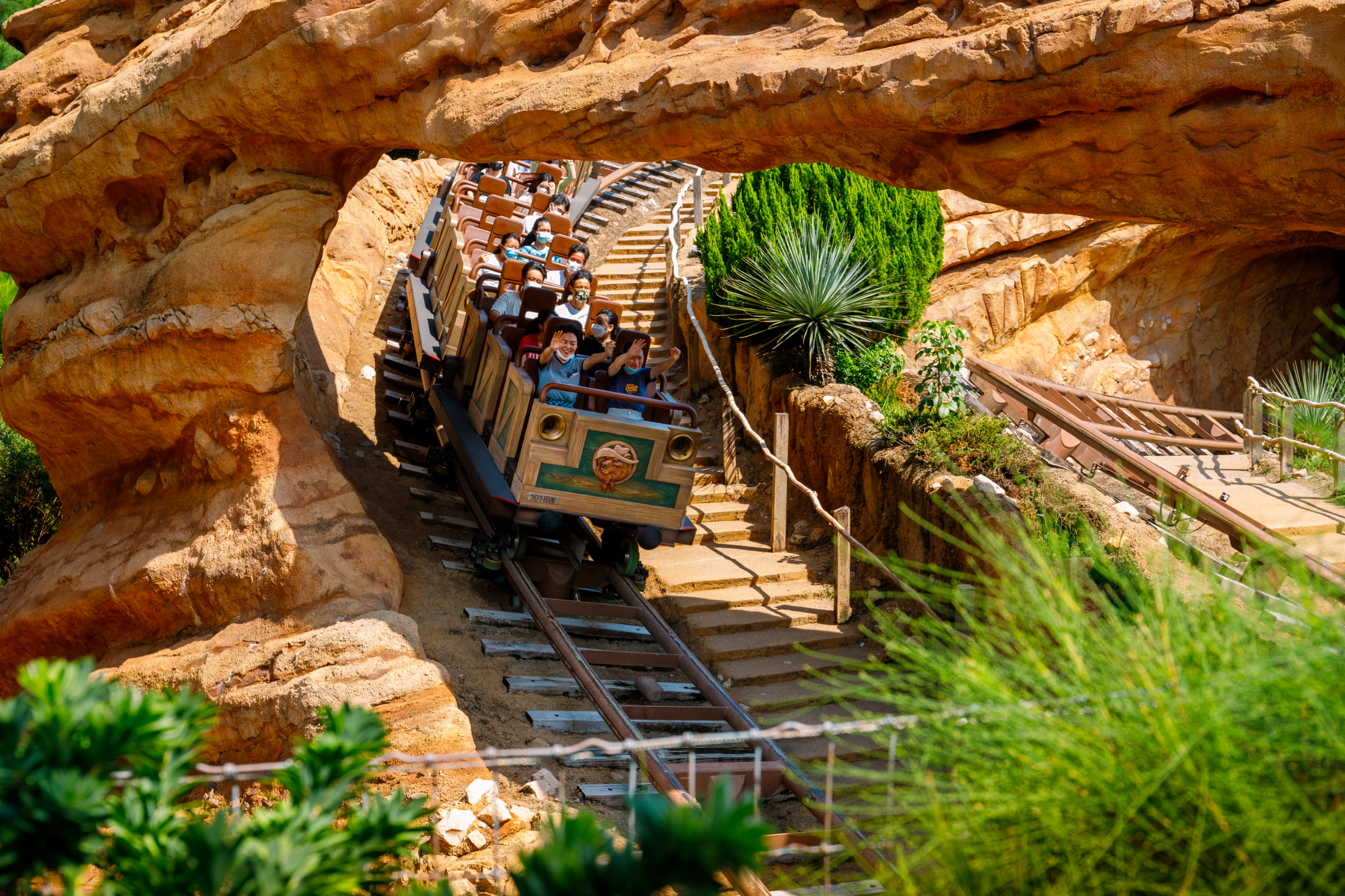 Roller coaster with passengers ascending a track, surrounded by rocky landscape