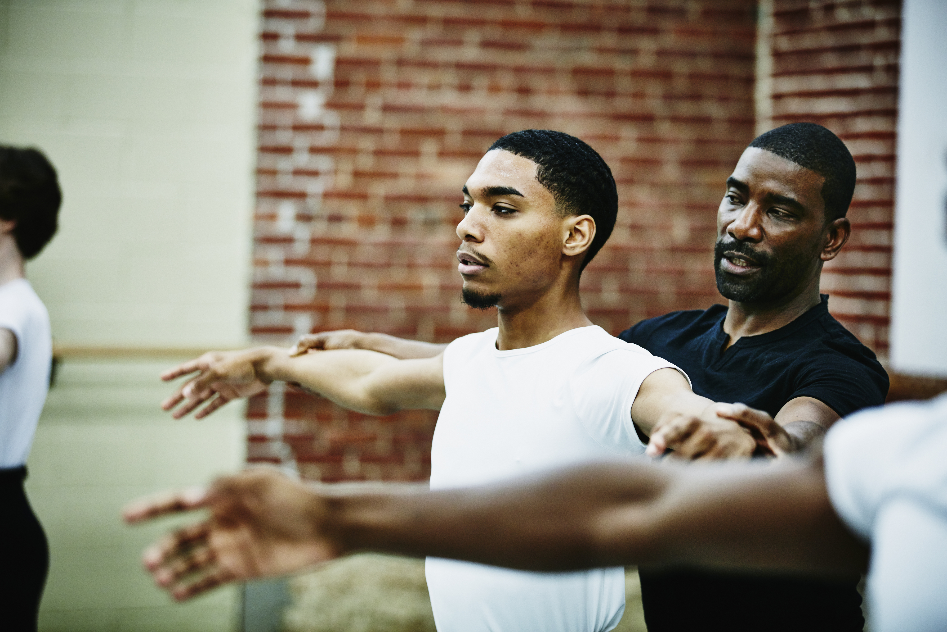 Two men practicing ballet with one man instructing the other, both focused and arms extended