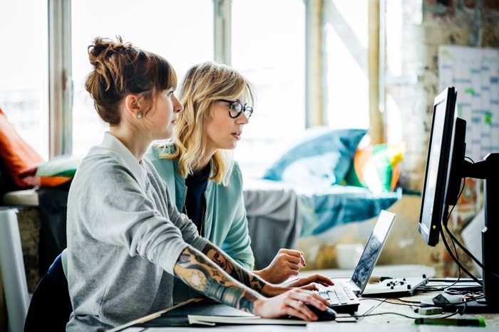 Two individuals working at a desk with computers. They are focused on the screens, engaging in a collaborative task