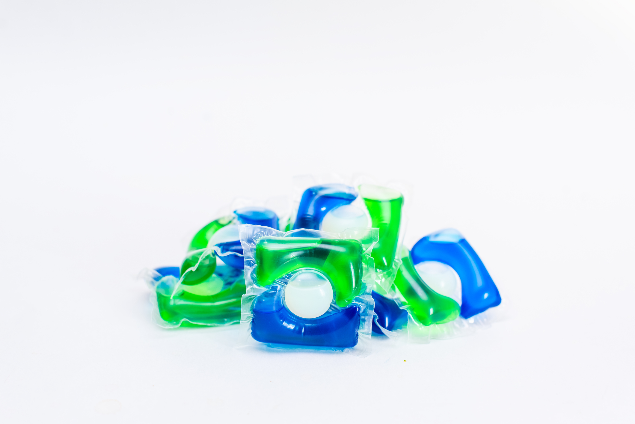 Pile of assorted laundry detergent pods on a plain background