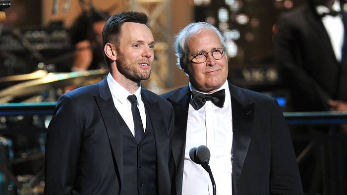 Joel McHale and Chevy Chase on stage, McHale in a bow tie, Chase in a long tie, presenting at an event