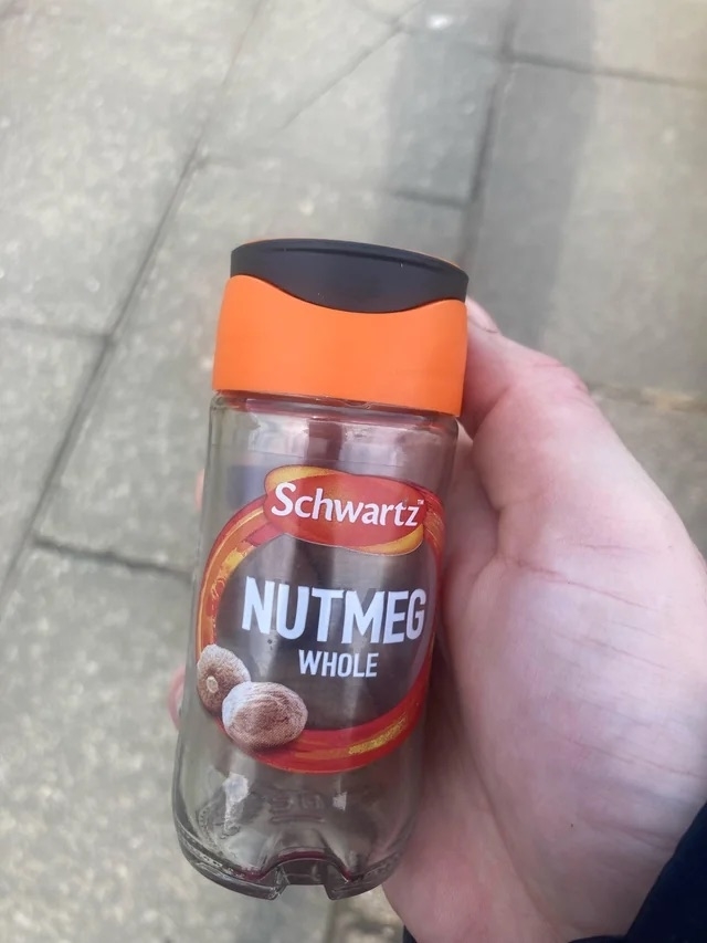Person holding a small jar of a Schwartz whole nutmeg spice jar with a red cap