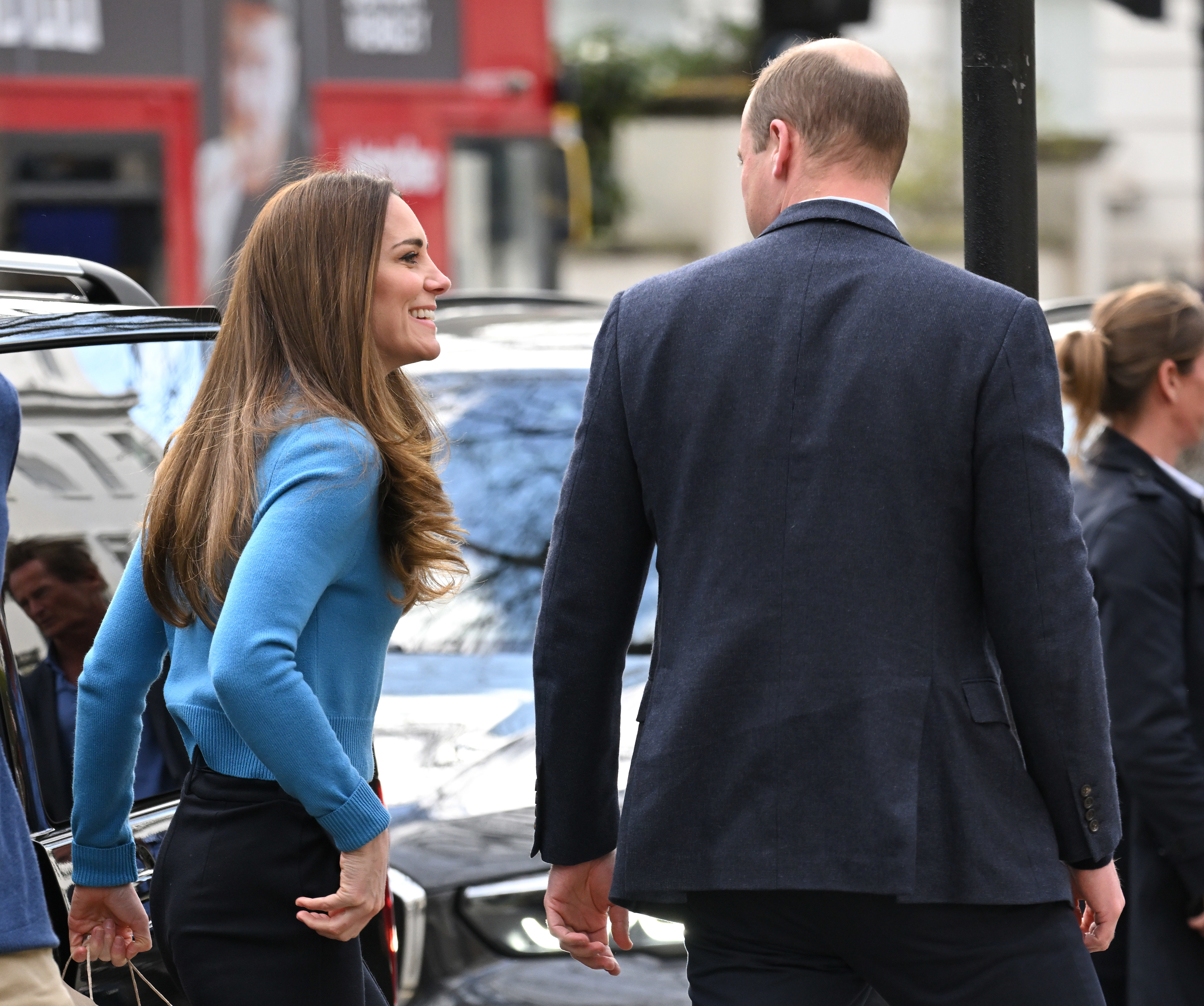 Kate Middleton in a sweater top and dark pants, walking with Prince William, viewed from behind