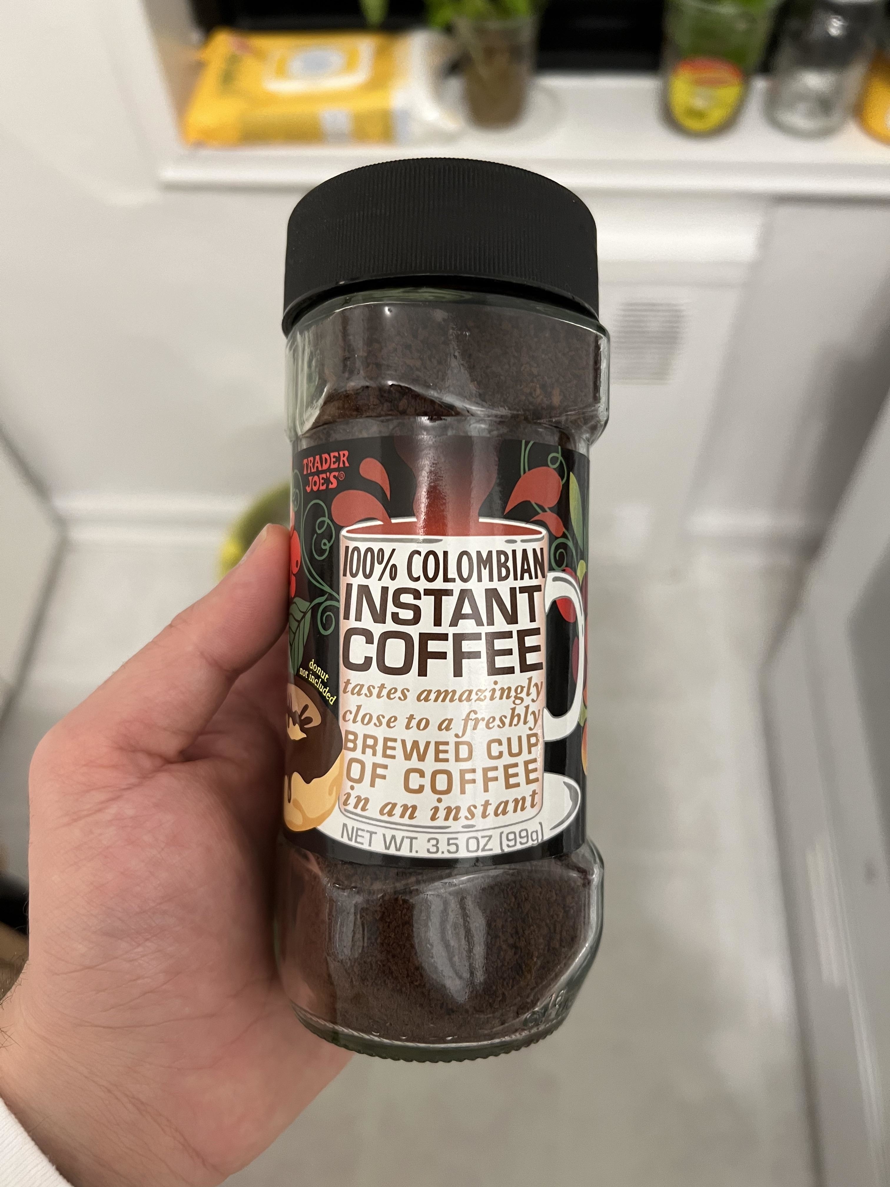 Hand holding a jar of Trader Joe&#x27;s 100% Colombian Instant Coffee in a kitchen