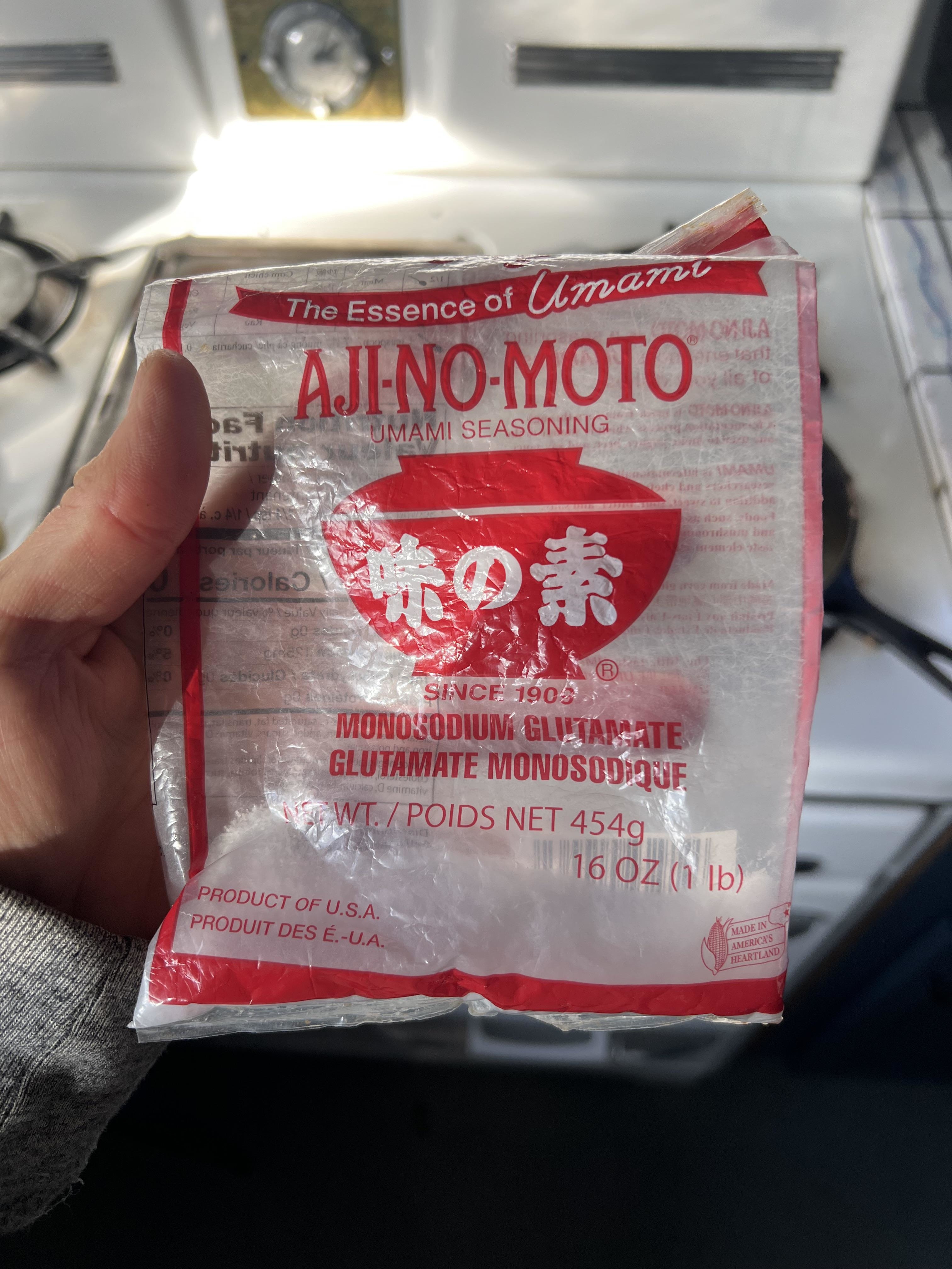 A hand holding a crumpled bag of umami seasoning made of monosodium glutamate