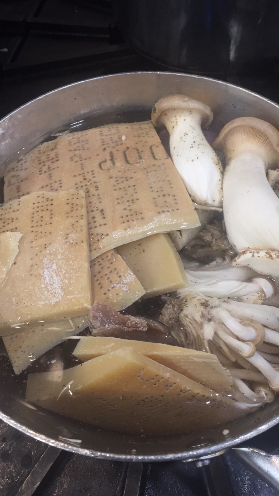 A simmering pot with various ingredients, including Parmesan rinds and mushrooms