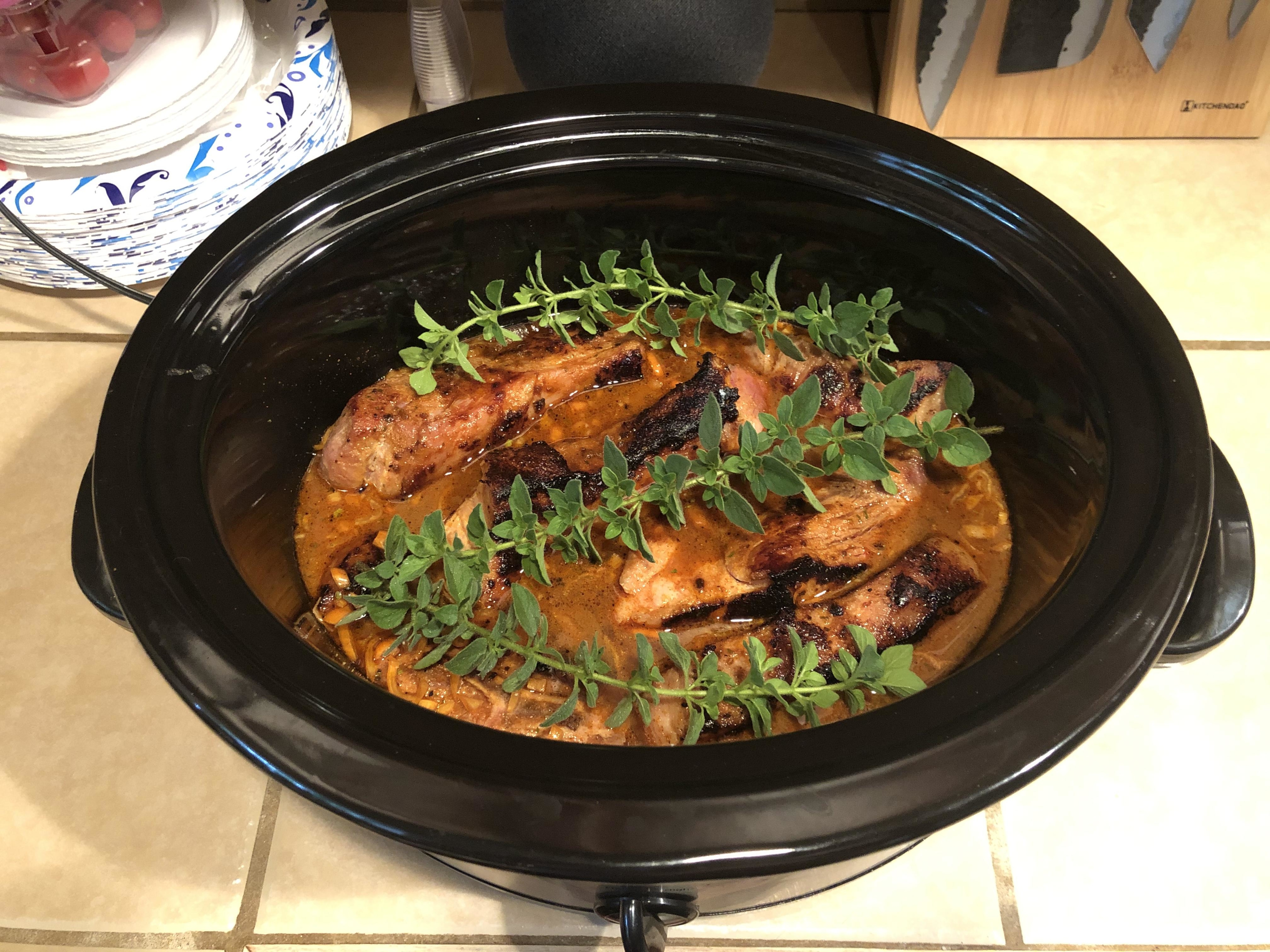 Pork ribs in a slow cooker garnished with fresh herbs