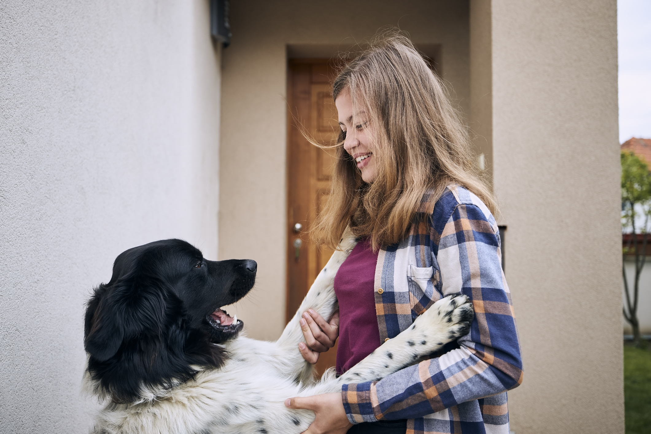 A smiling person standing, interacting with a happy dog by a house entrance