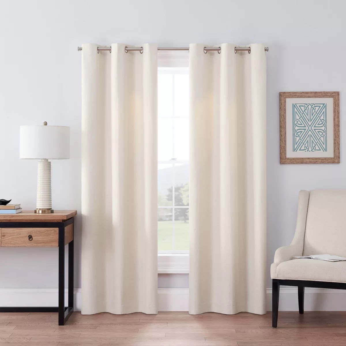 Cream-colored curtains hanging on a rod beside a beige armchair and a wooden side table with a lamp