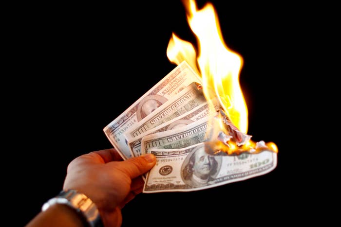 Hand holding burning dollar bills, symbolizing financial loss or waste