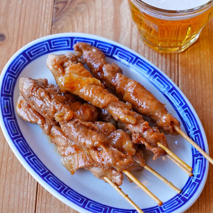豚の串焼きが皿に盛られており、隣にはビールが置かれています。