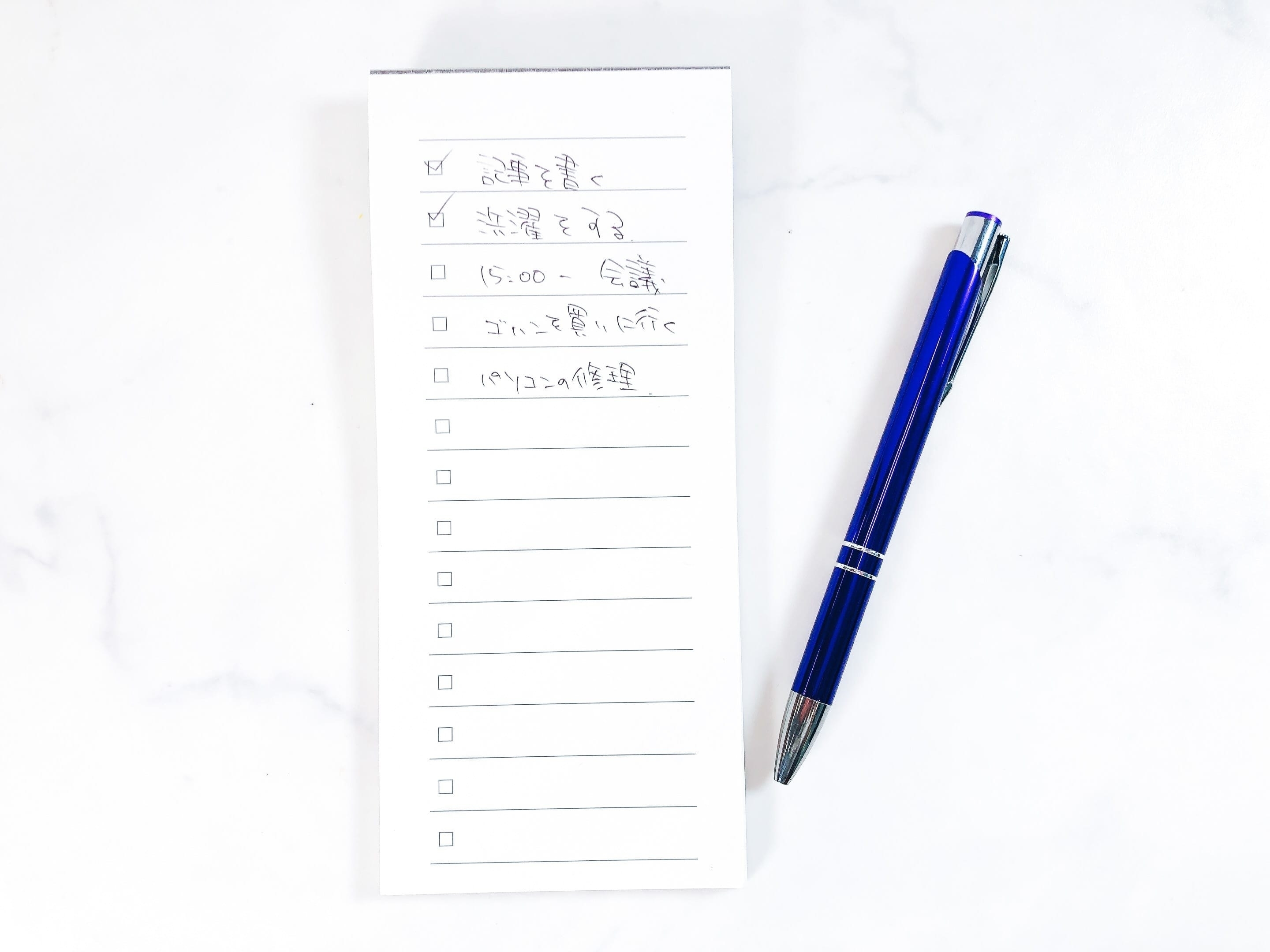 手書きの文字が書かれたリストと青いペンが置かれた白い背景。