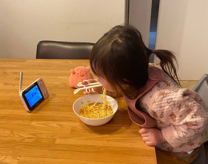 小さな女の子が食事をしながらビデオを見ています。