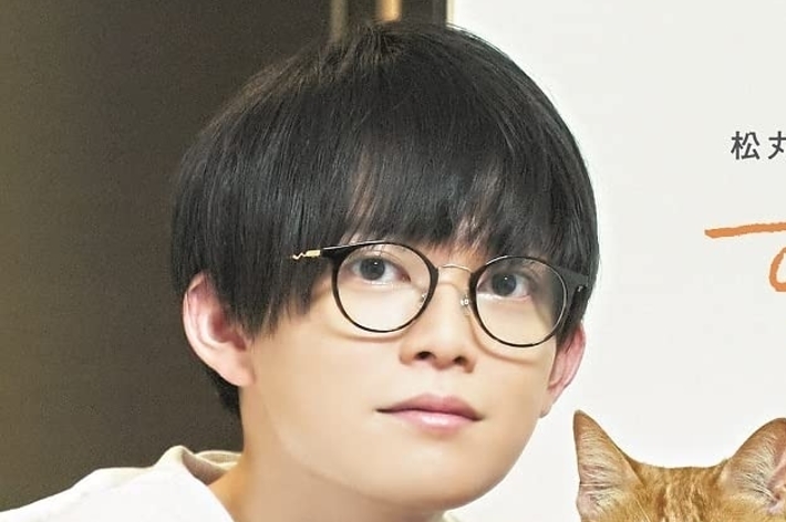 若い男性と茶色の猫が一緒にいるポスター。男性はメガネをかけており、猫とカメラを見つめている。