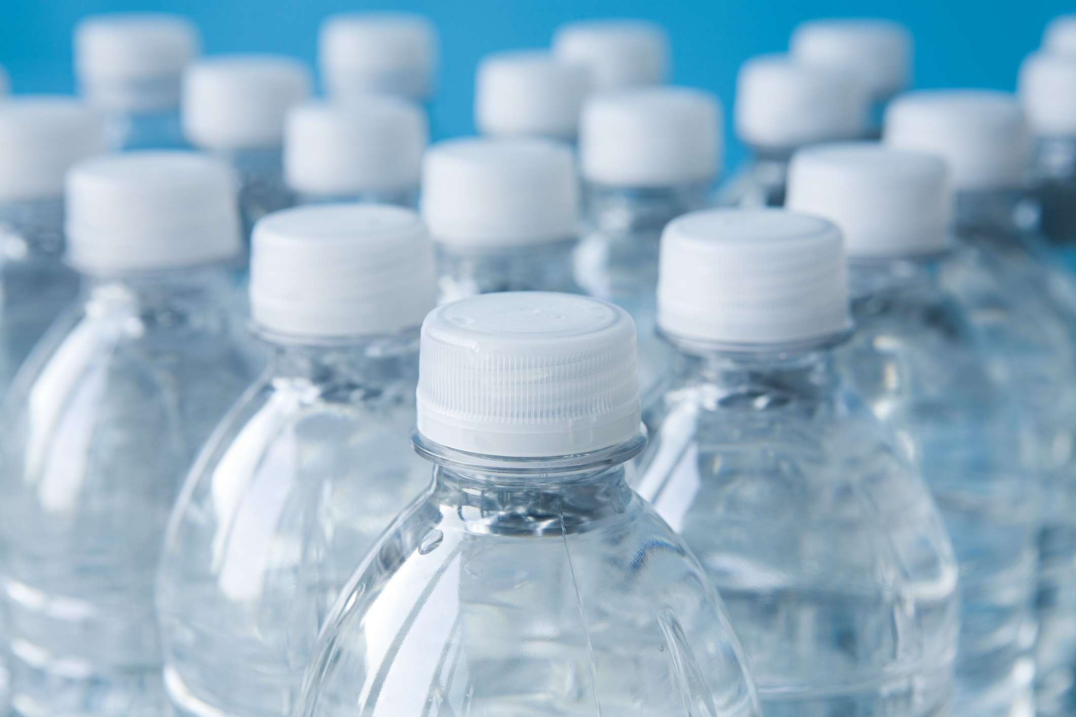 Several clear water bottles with white caps against a blue background