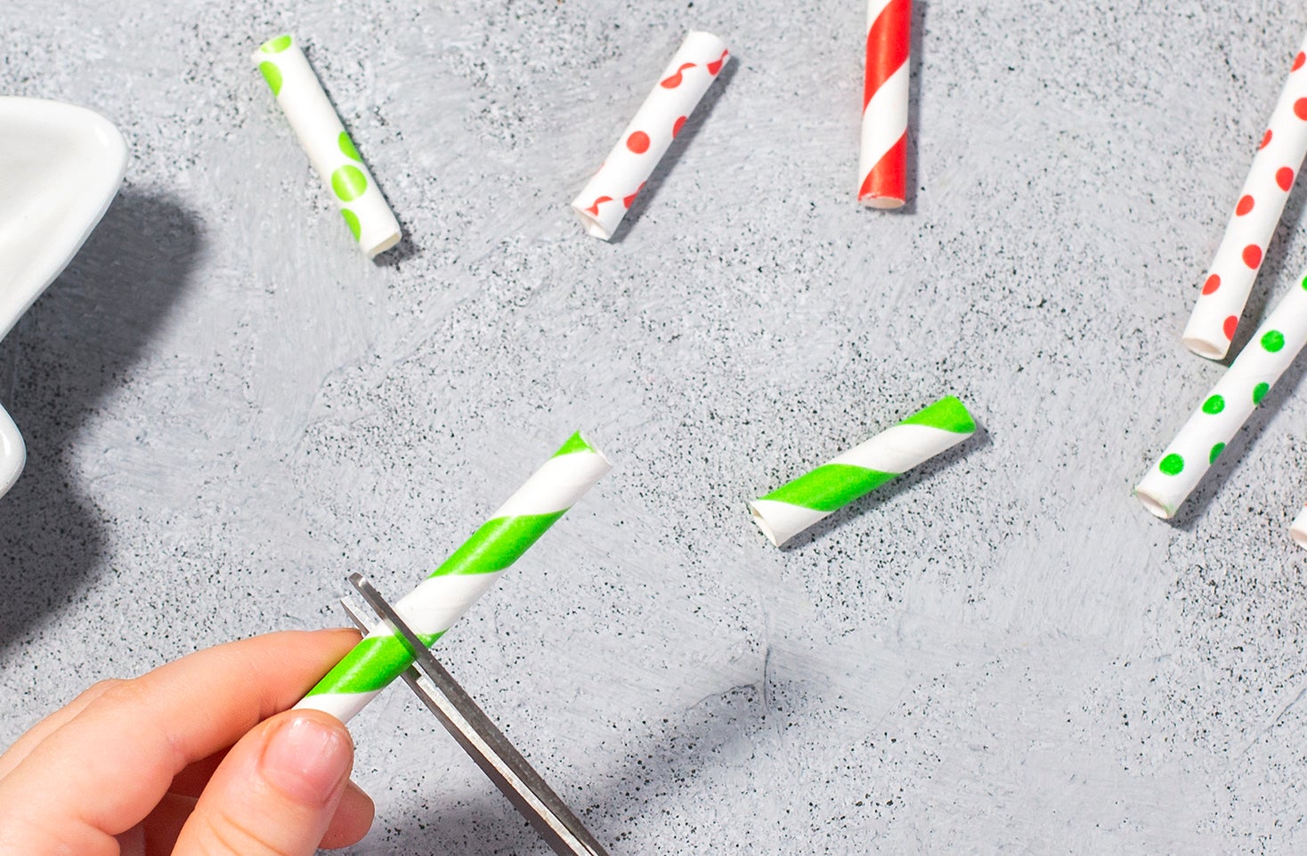 Hands cutting a plastic straw, with various straws and a dish on the table