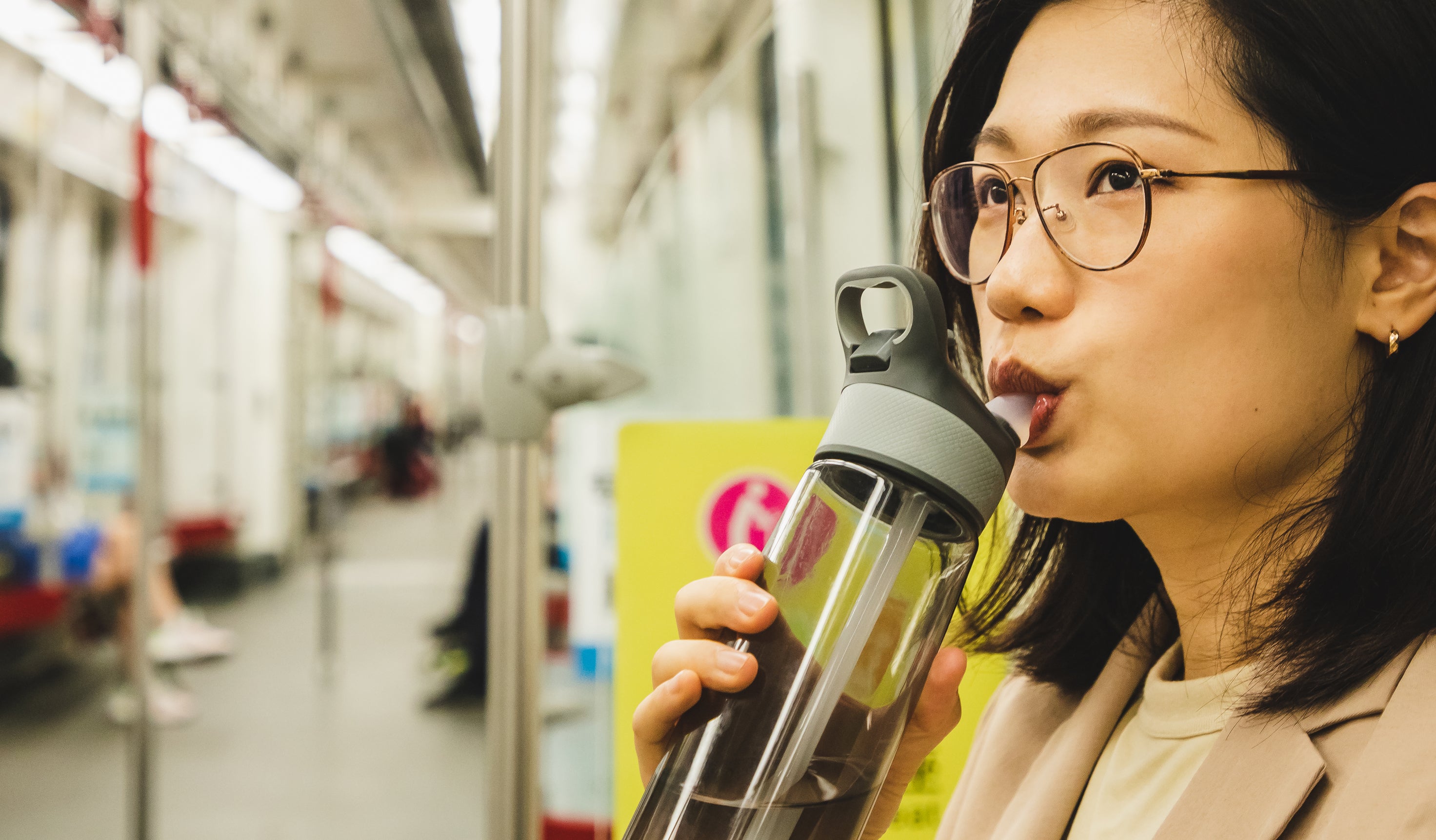 Woman drinking from a bottle on a subway train, passengers seated in background