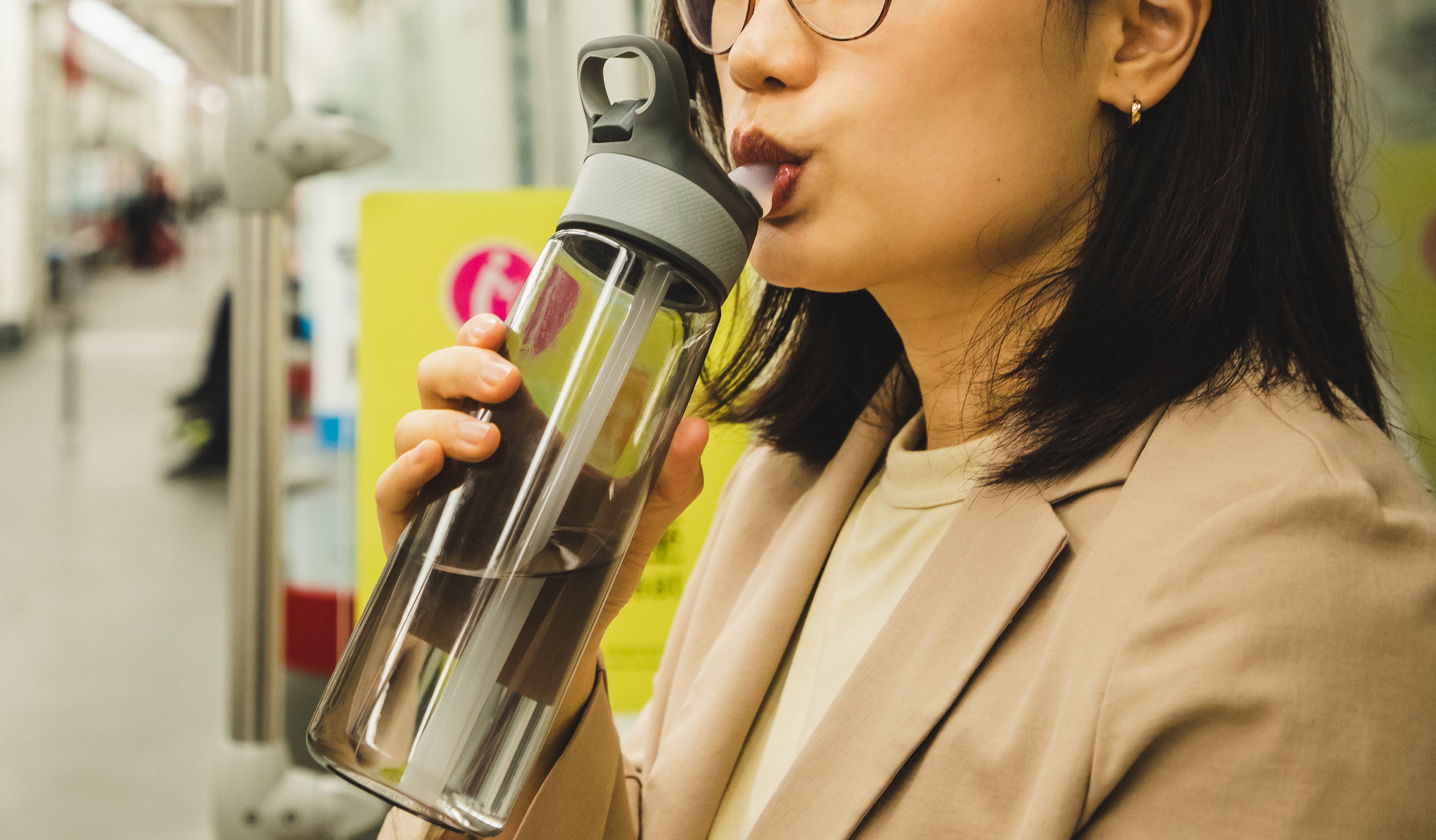 Woman drinking from a bottle on a subway train, passengers seated in background