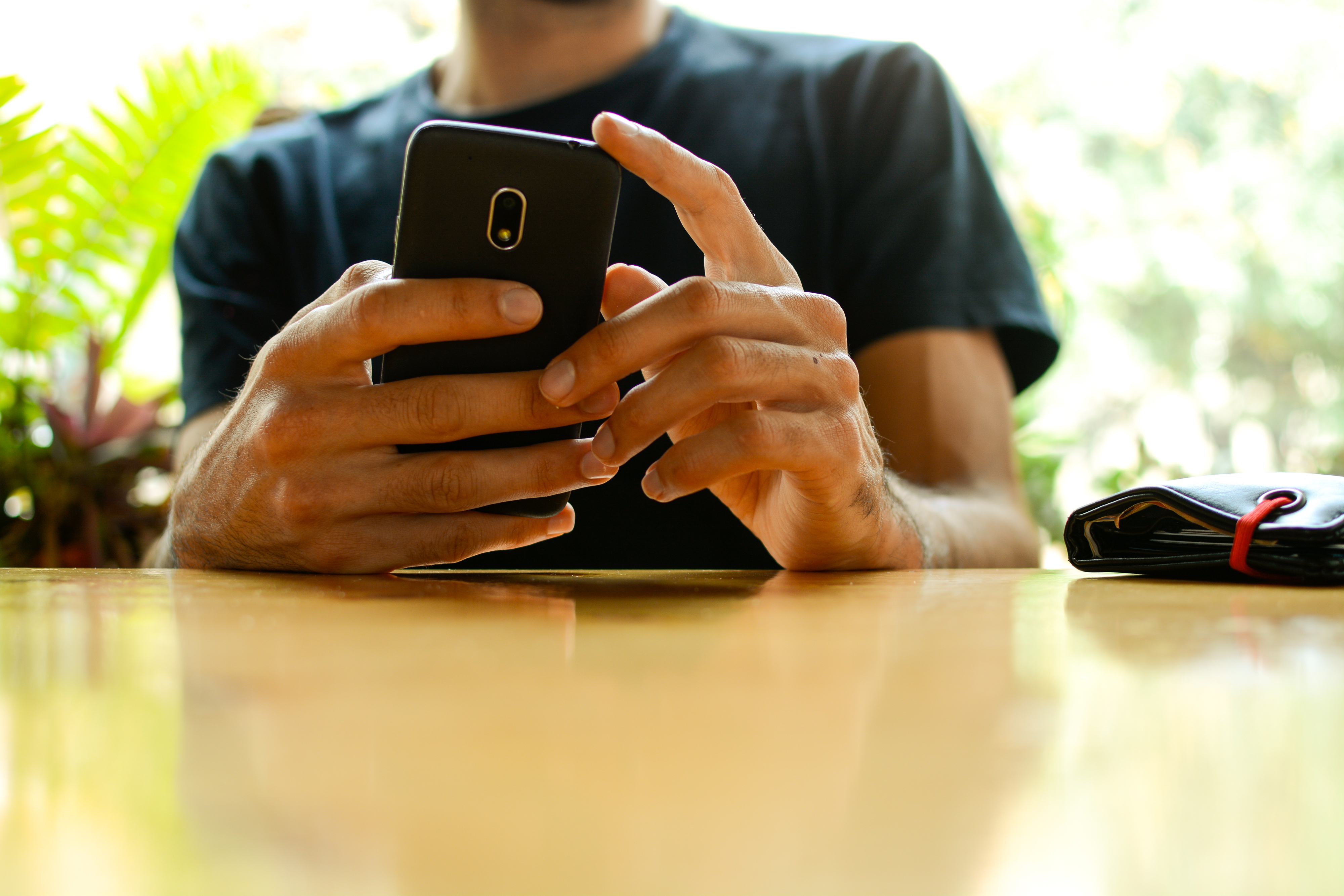 Person using a smartphone, resting on a table, with a wallet beside them