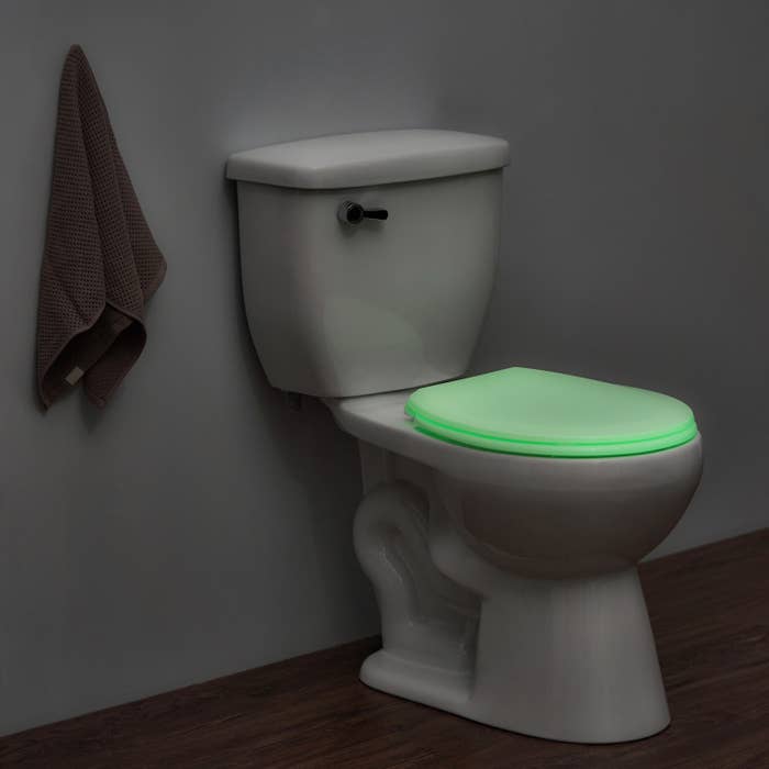 Toilet with a glowing green seat in a dimly lit bathroom
