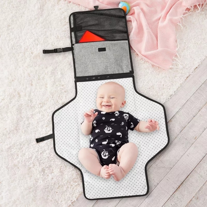 Baby lies on an open diaper bag with built-in changing pad, smiling joyfully