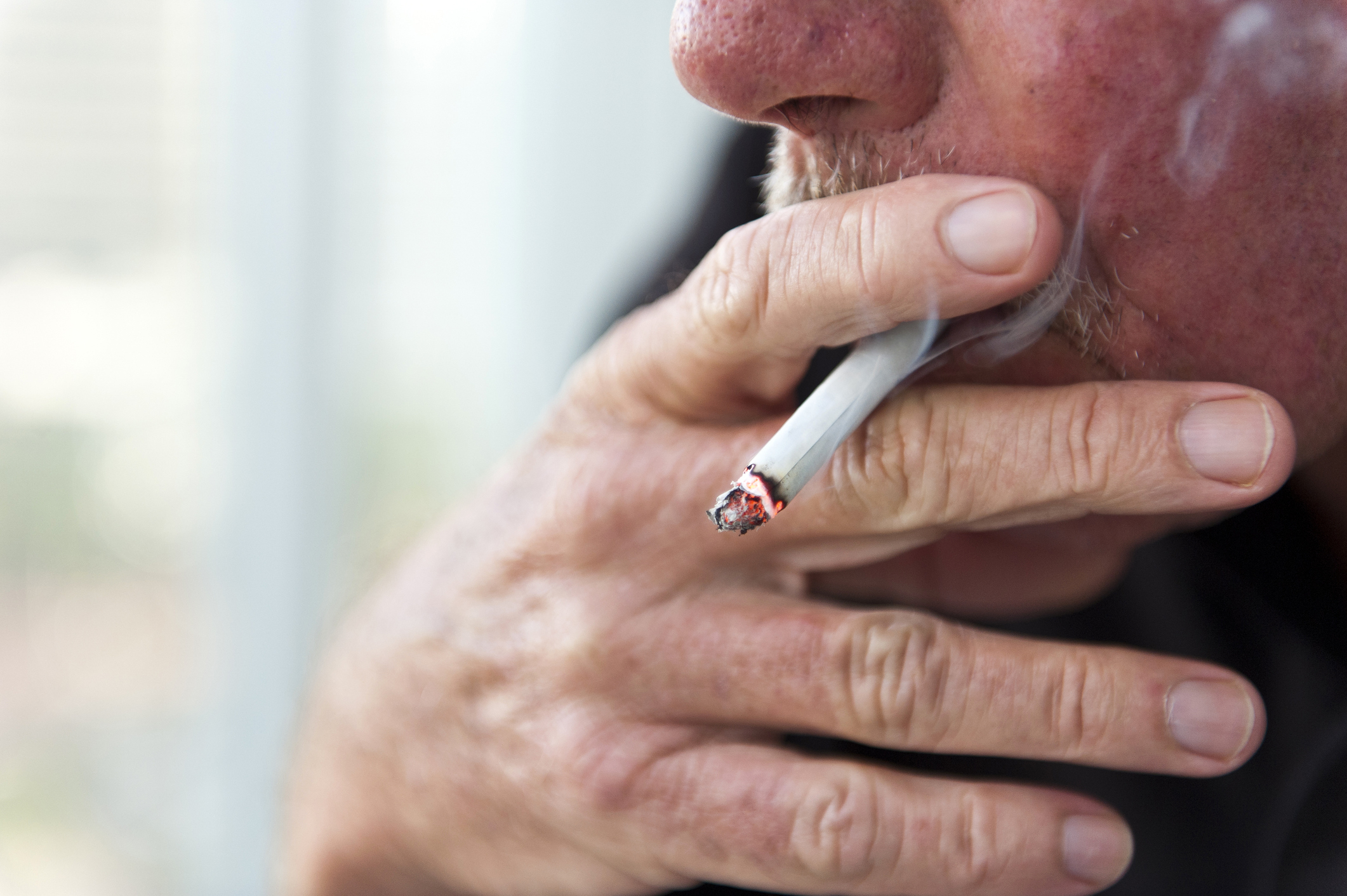 Person smoking a cigarette, close-up of hand and mouth, focus on lit end