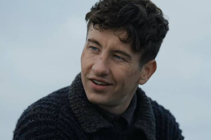 Man with curly hair wearing a sweater, looking off to the side, slight smile