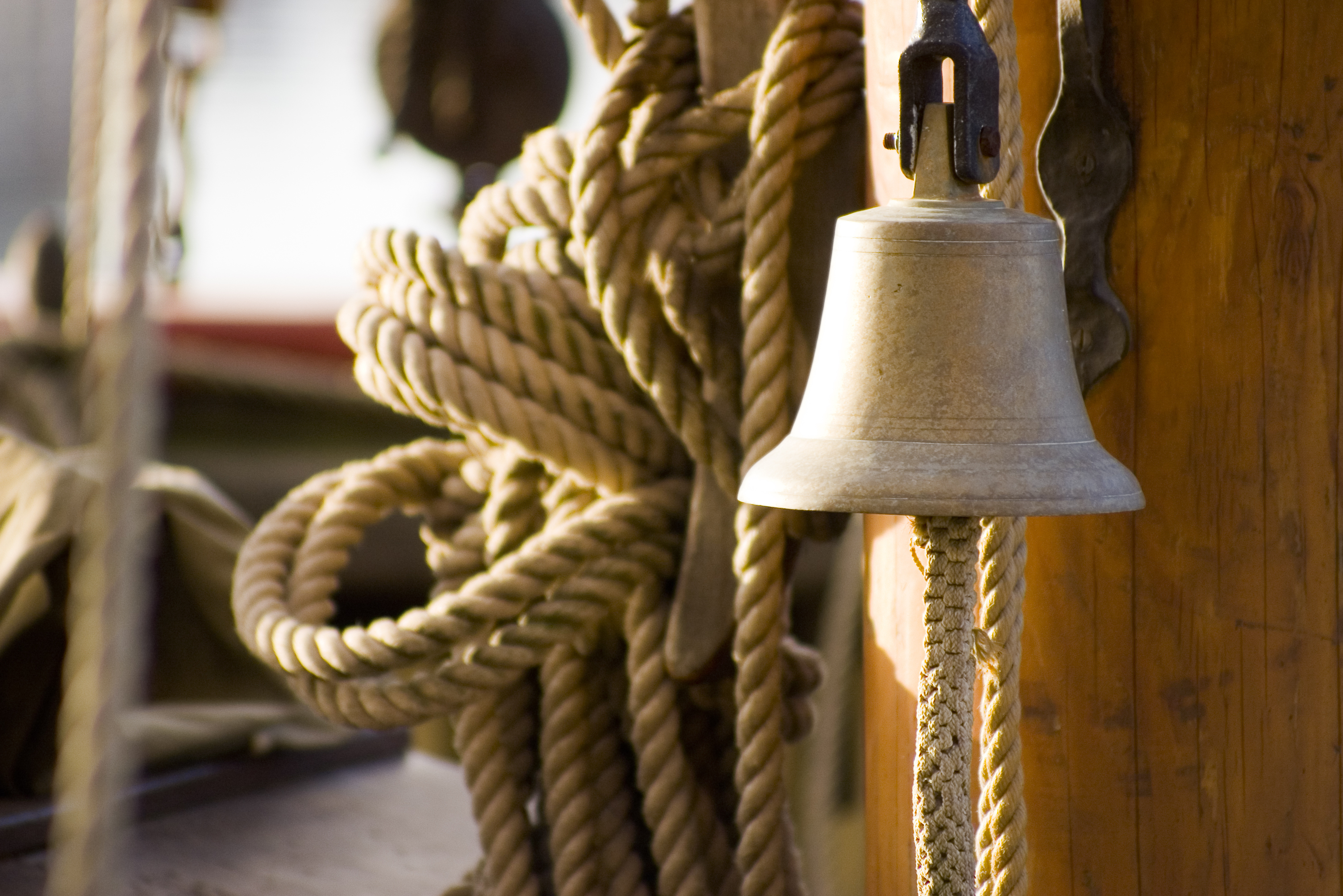 Ship&#x27;s bell attached to a wooden surface with coiled ropes on the sides