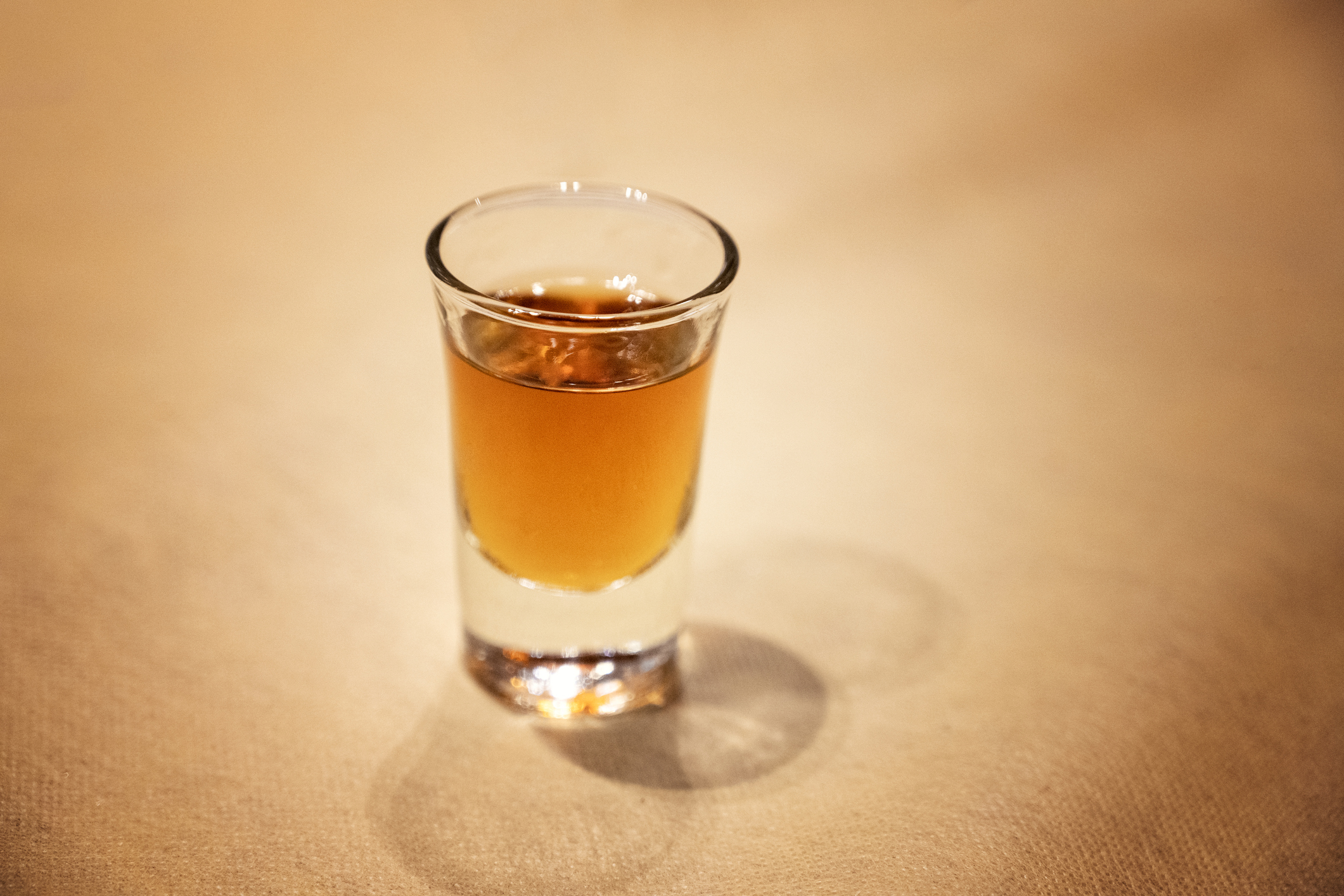 Shot glass filled with amber liquid on a textured surface