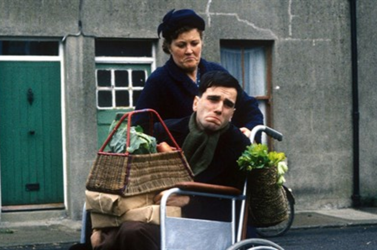 Man in a wheelchair with a basket of groceries, accompanied by a woman standing behind him
