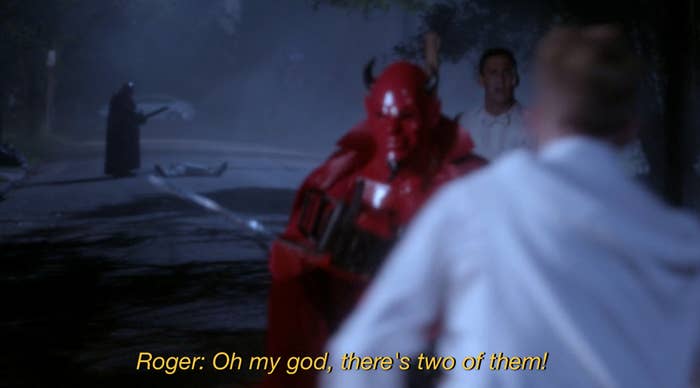 Scene from a show with a character in a red costume, another person behind, and a subtitle text