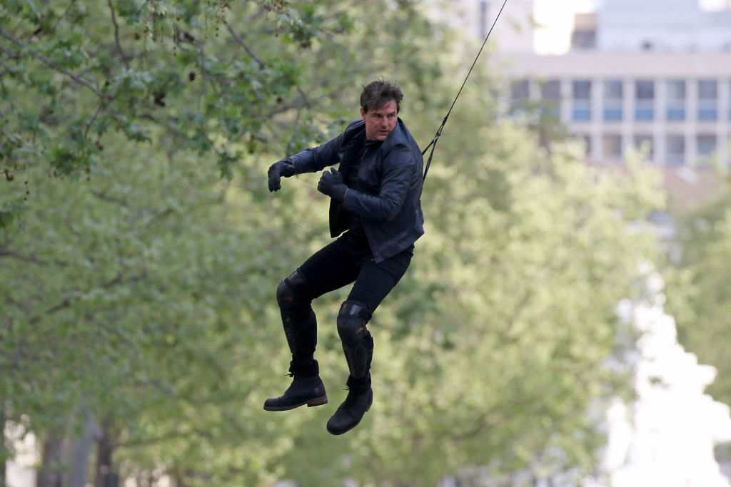 Man in a jacket and jeans performs a zip line stunt outdoors