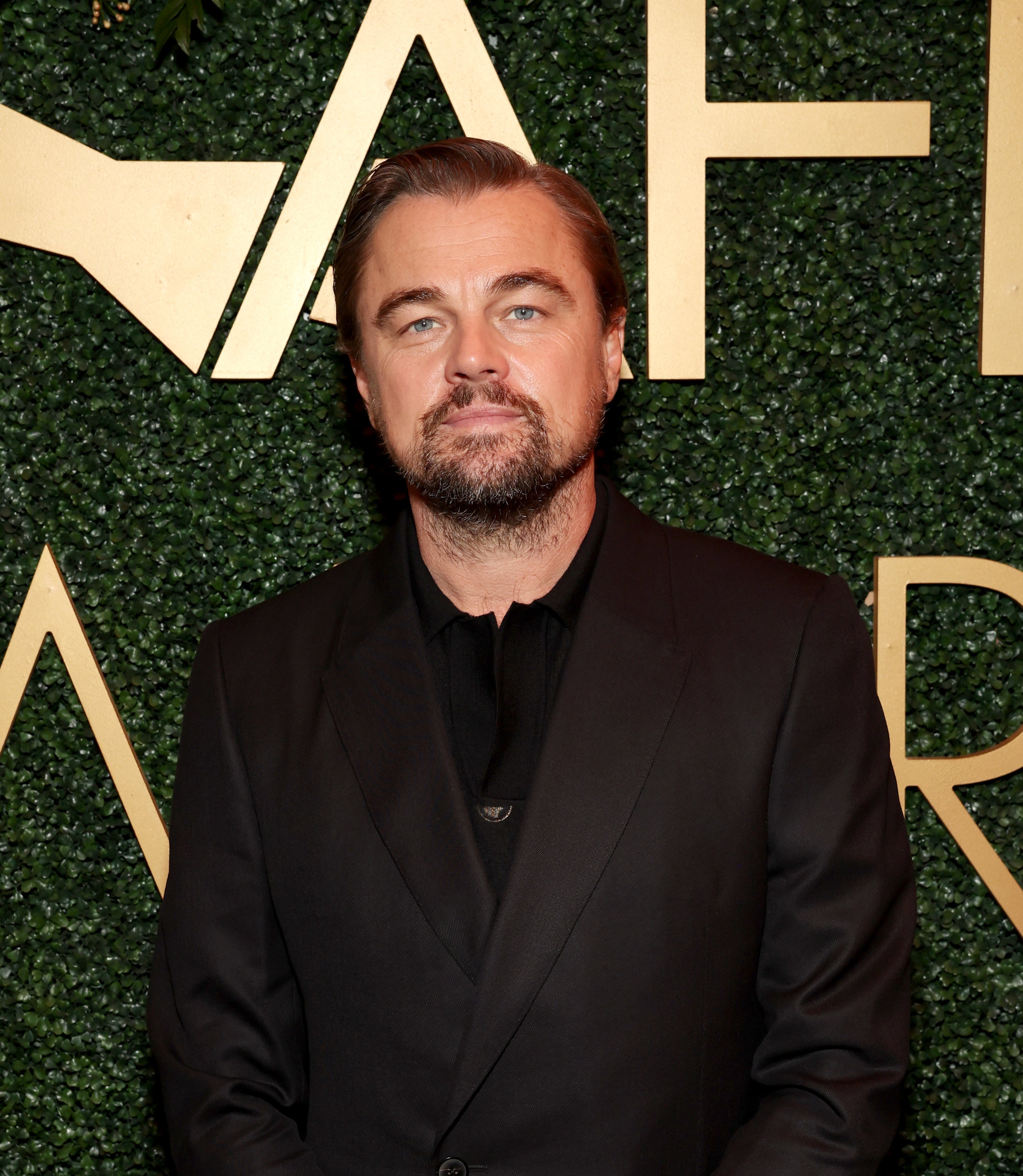 Leonardo DiCaprio in a black suit at the AFI Awards against a floral backdrop