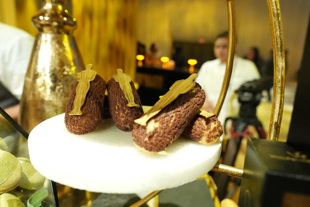 Gourmet chocolate eclairs displayed on a stand with chefs in the background
