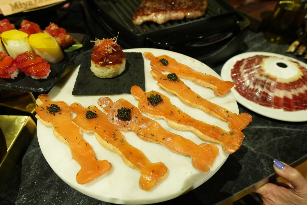 Plate of assorted sushi and sashimi including salmon and tuna on a dining table, with a person holding the plate