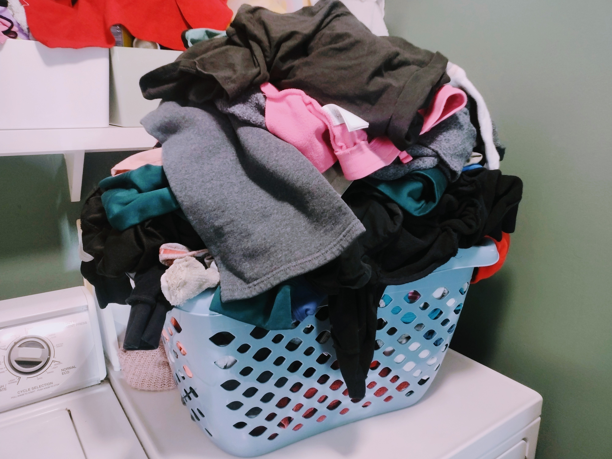 A laundry basket overflowing with assorted clothes, atop a washing machine